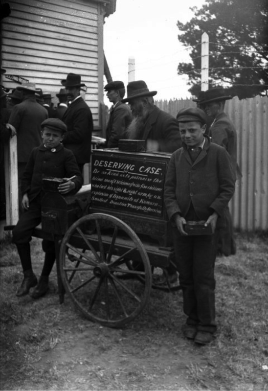 Jack (right) and Rudolph Lousich collecting donations for their father Louis Lousich. The sign reads: Deserving Case. Be so kind as to patronise the blind man a widower with five children who lost his sight and right arm by an explosion of dynamite at Kumara. Smallest donation thankfully received.